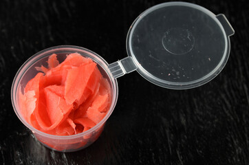 Ginger root chopped into thin slices of red color in a delivery plastic jar.