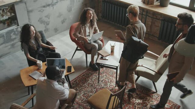Top-view slowmo of group of young multi-ethnic business partners meeting for discussing new project in modern loft-style coworking space