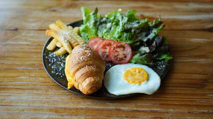 Vegetarian croissant with cheese and porched egg with french fries and vegetable. Healthy European breakfast