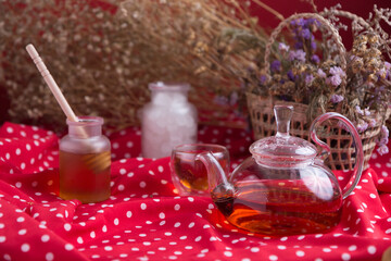 Tea pot and tea cup on wood table with honey and suagr in mag with flower basket on red cloth...