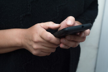 Hands holding a smartphone or mobile phone using social media apps to chat. Black clothes in the background