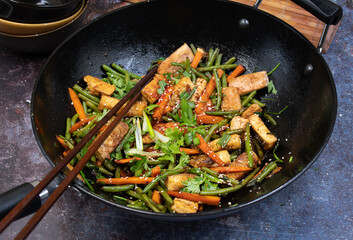 Vegan tofu, beans andcarrot stir fry in black wok, chopsticks