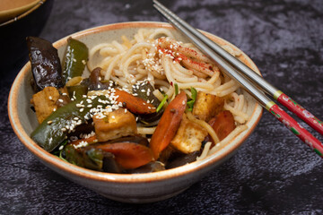 Vegan Stir fried eggplant; carrot and pepper served with rice noodles in bowl; with chop sticks