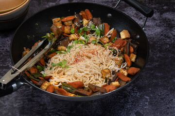 Vegan Stir fried eggplant, carrot and pepper served with rice noodles in cast iron wok