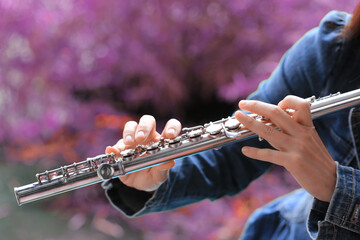 Flute classical instrument player playing song. Instructor practicing bronze woodwind for orchestra as solo with green bokeh outside with nature.