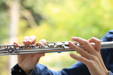 Flute classical instrument player playing song. Instructor practicing bronze woodwind for orchestra as solo with green bokeh outside with nature. - obrazy, fototapety, plakaty