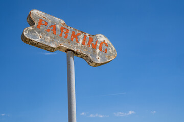 Old rusty generic parking sign with an arrow against a blue sky