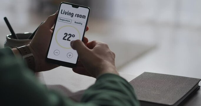 man is using modern app in smartphone for controlling parameters of smart home system, closeup view of screen