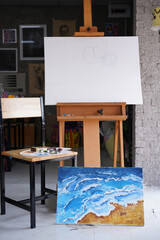 Acrylic sea and beach painting on drawing stand with palette and brush. Blue wave on golden sand hand painting with brush and knife palette technique. Art on canvas.