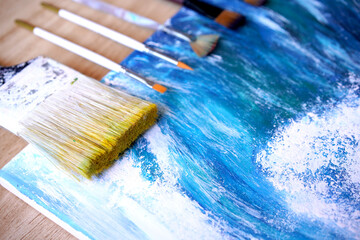 Painter paint acrylic on canvas with brush with blue ocean on frame. Artwork as hobby or occupation for artist. Big wave in sea w creates artwork by mix color and decors picture as hard copy art. - obrazy, fototapety, plakaty