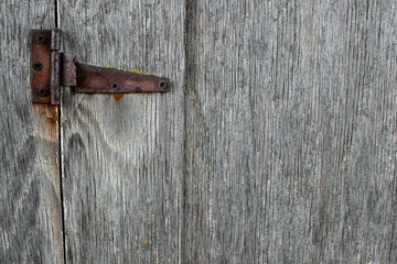 A gray wooden door with a small rusty hinge.