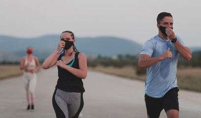 Multiethnic runners group wear face masks running keep social distance outdoor. Fit healthy diverse team wears sportswear jogging in evening on nature sports track distancing for safety.