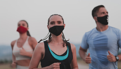 Multiethnic runners group wear face masks running keep social distance outdoor. Fit healthy diverse team wears sportswear jogging in evening on nature sports track distancing for safety.