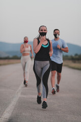 Multiethnic runners group wear face masks running keep social distance outdoor. Fit healthy diverse team wears sportswear jogging in evening on nature sports track distancing for safety.