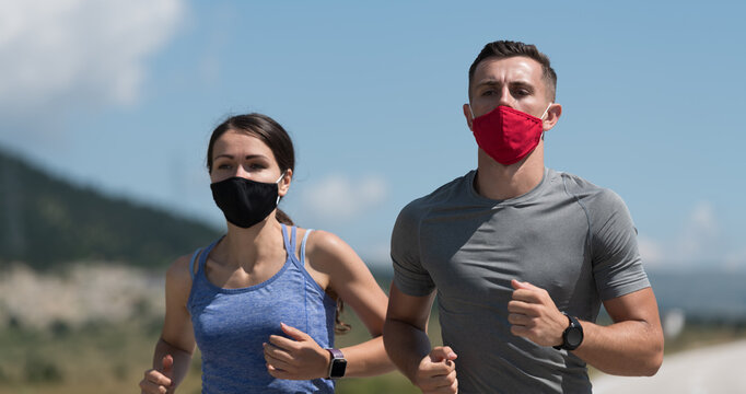 Young man and woman in protective masks running and doing exercises outdoors in the morning. Sport, Active life Jogging during quarantine. Covid-19 new normal. Selective focus.