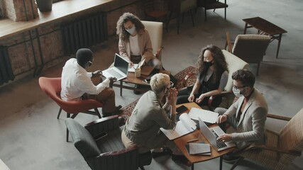 Top-view slowmo of young multi-ethnic business partners in face masks brainstorming in loft coworking workspace then giving high-fives to each other after success in project - Powered by Adobe