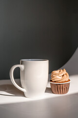 A cupcake or muffin stands next to a cup of coffee.