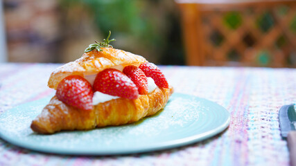 Croissant with strawberry and white softly mousse cream on blue ceramic plate with icing. French dessert assorted red berry.