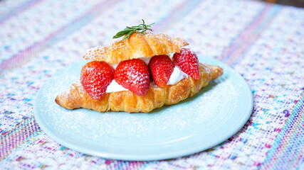 Croissant with strawberry and white softly mousse cream on blue ceramic plate with icing. French dessert assorted red berry.