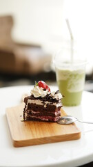Chocolate cake sliced on wood plate with cold green tea milk in plastic cup in coffee shop.