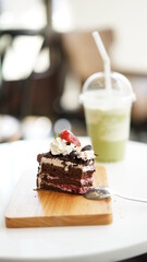 Chocolate cake sliced on wood plate with cold green tea milk in plastic cup in coffee shop.