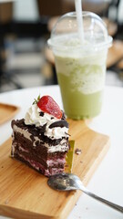 Chocolate cake sliced on wood plate with cold green tea milk in plastic cup in coffee shop.