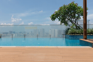 modern rooftop residential swimming pool on a beautiful sunny day. The pool is surrounded by wooden decking and features lush plants and views of city skyline