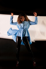 vertical portrait of a curly model wearing a blue dress and black latex pants with black and white paper like background