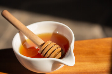 Honey with dipper in small white bowl. Homemade honey with wooden stick in sunlight. Honey in jar. Natural sweetener. Healthy nutrition. Natural dessert concept. Sweet food.