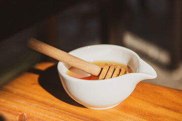 Honey with dipper in small white bowl. Homemade honey with wooden stick in sunlight. Honey in jar. Natural sweetener. Healthy nutrition. Natural dessert concept. Sweet food.