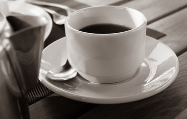 White cup of black coffee, sepia tone. Mug of coffee on the table with unfocused foreground. Aromatic hot drinks.Weekend mood. Breakfast concept. Morning in big city lifestyle. 