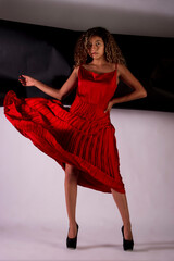 vertical portrait of a latin woman posing and wearing a red elegant dress with black and white paper like background