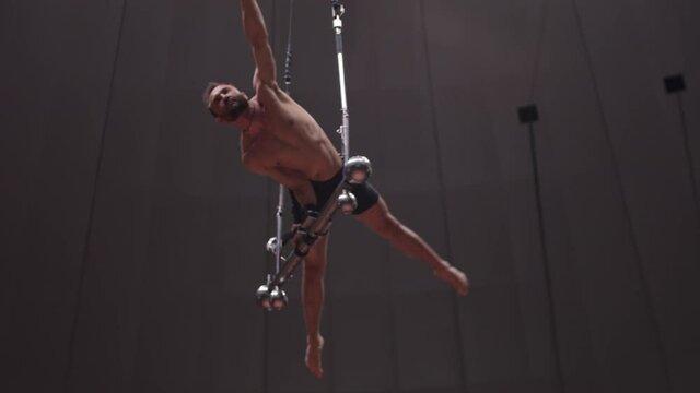 Acrobatic bearded man standing on hands on performance construction at the circus arena