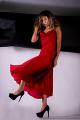vertical portrait of a latin woman posing and wearing a red elegant dress with black and white paper like background