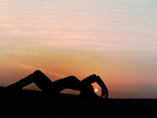 Woman silhouette yoga exercises on beach during sunset.