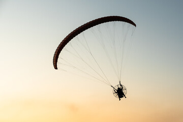 Silhouette of a man flying free on a paraglider at sunset, on a golden clear sky with copy space