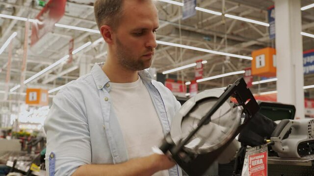 Man chooses a circular saw in a tool shop. Male select a product in a hardware store.