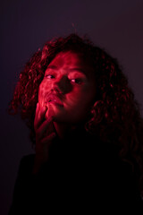 vertical portrait of a young latin woman posing with red ligth and dark background