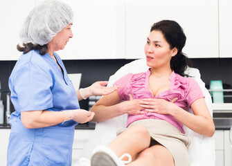 Interested asian woman consulting with professional cosmetologist about possible breast...