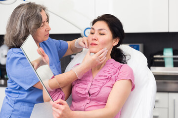 Highly qualified cosmetology doctor carefully examines the face of a young woman patient before the mesotherapy ..procedure