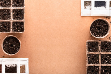 Biodegradable peat pots and trays full of potting soil made of peat, worm humus and perlite, and many vegetable seeds in small envelopes ready for sowing, on a raw surface with copy space