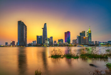 Obraz premium Riverside city sunset moments in the sky at end of day brighter coal sparkling skyscrapers along beautiful river in Ho Chi Minh City, Vietnam