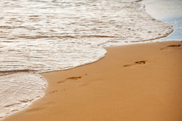 Footprints at golden sand, footsteps. Sea background, nature of tropical summer beach with rays of sun light. Sand beach, sea water with copy space, summer vacation concept.