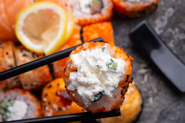 sushi roll with soft cheese holding by sticks. sushi rolls served at grey  tray. flat lay. close up