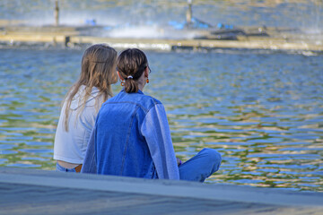 Two girls sit on the city embankment on a summer day