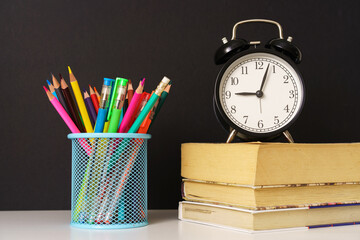 the alarm clock stands on the books and glass with pencils on black background, concept back to...