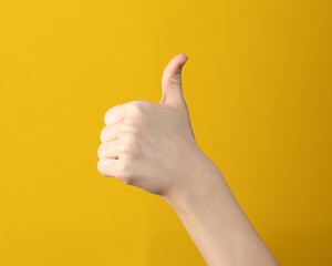 hand gesture with closed fist held with and thumb extended upward on yellow background. Signal of approval, symbol, sign of perfect or accept.