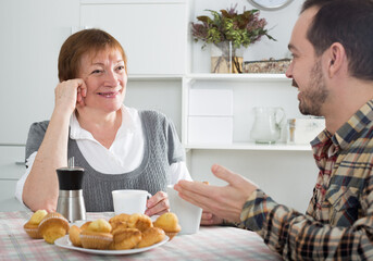 Elderly mother and son together having breakfast at table and friendly communicate