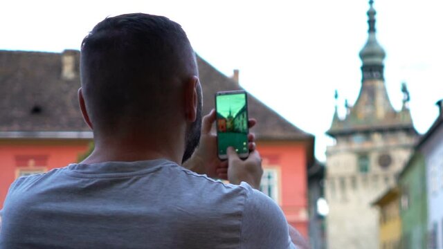 Young man taking photo with smartphone of old town in Romania