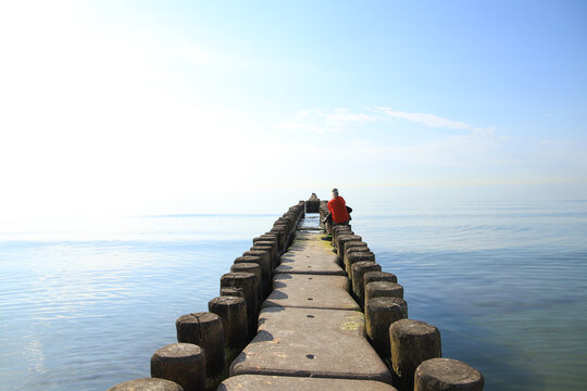 A man is sitting on groynes and waits for the sunset at the baltic sea, Germany